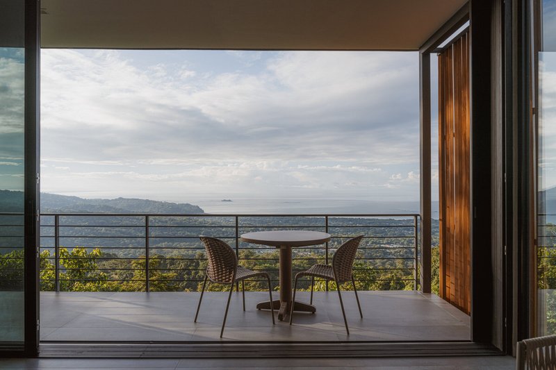 Open sliding doors framing a balcony terrace with metal railing and distant mountain view