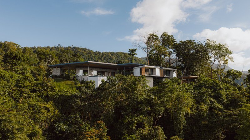 Distant view of the residence perched on a forested slope under afternoon clouds