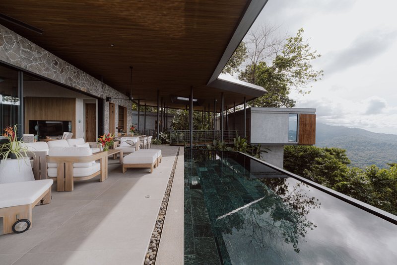 Covered terrace with infinity pool, timber ceiling, stone wall, and mountain vista beyond