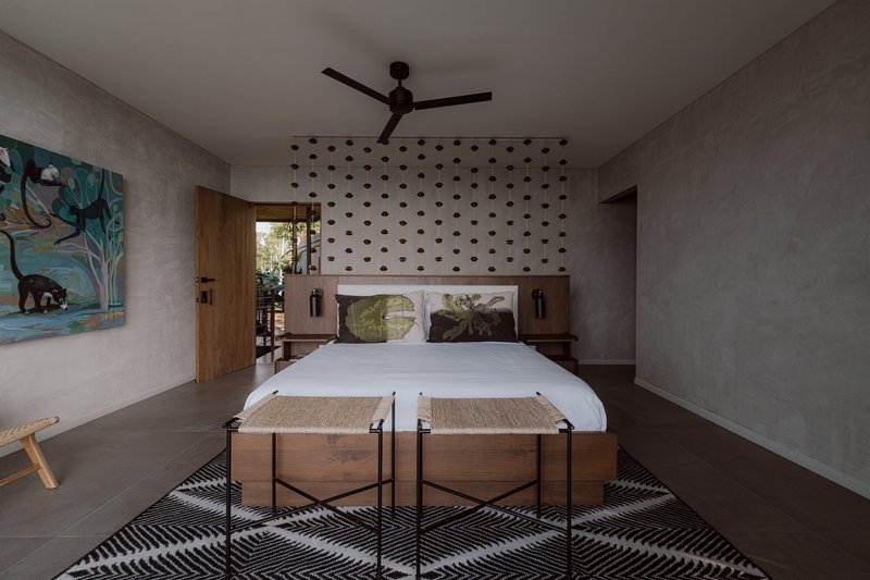 Bedroom with perforated concrete headboard wall, timber door, and polished concrete floor