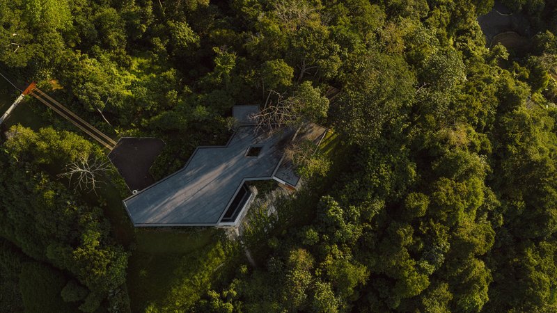 Aerial view of the angular roof nestled within dense jungle canopy on a hillside