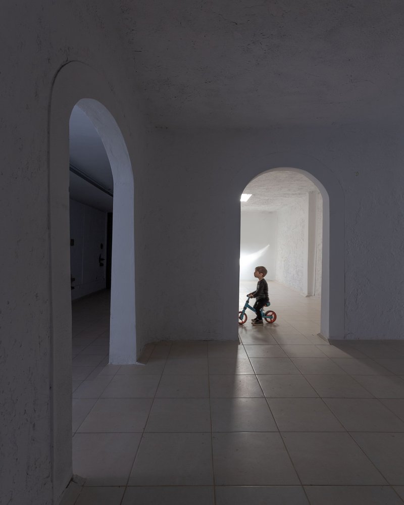 Tiled passage with rounded arched openings and child on tricycle in sunlit doorway