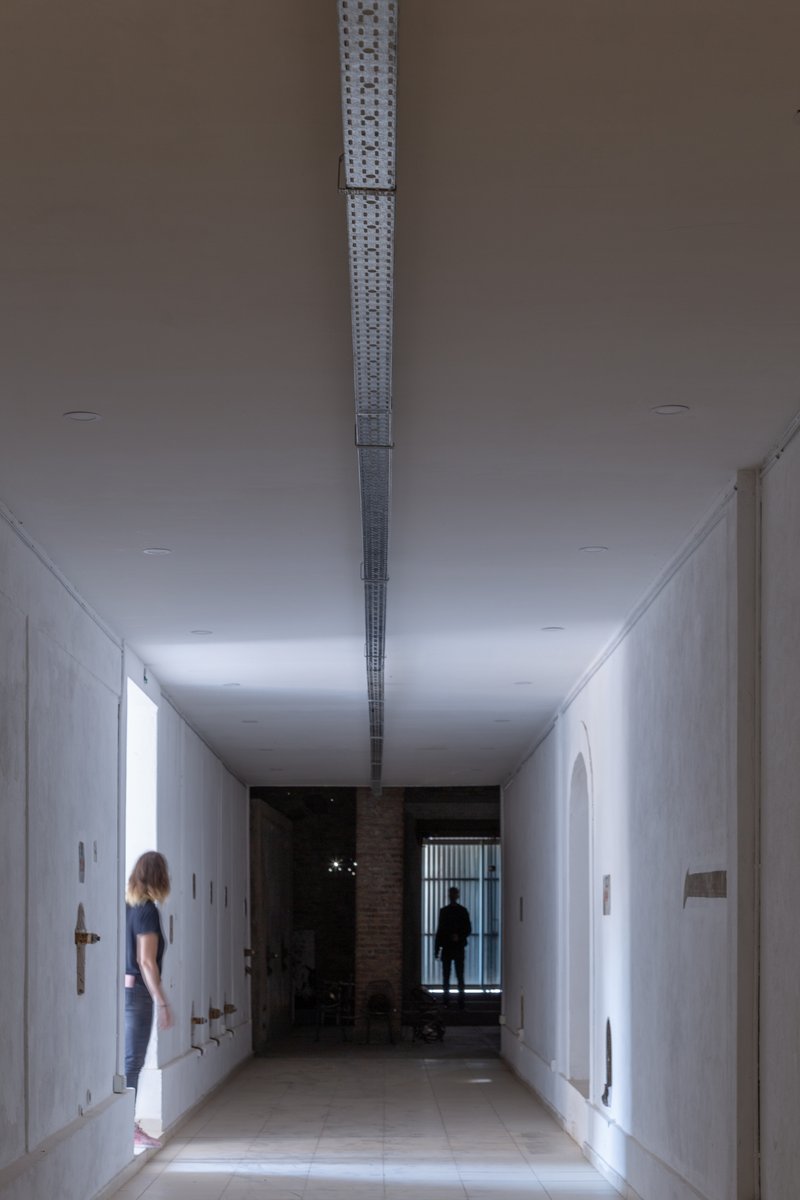 Long white corridor with perforated metal skylight running along the ceiling center and two figures
