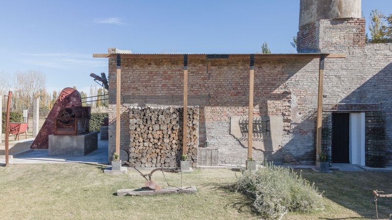 Timber-framed canopy sheltering stacked firewood against the weathered brick factory wall