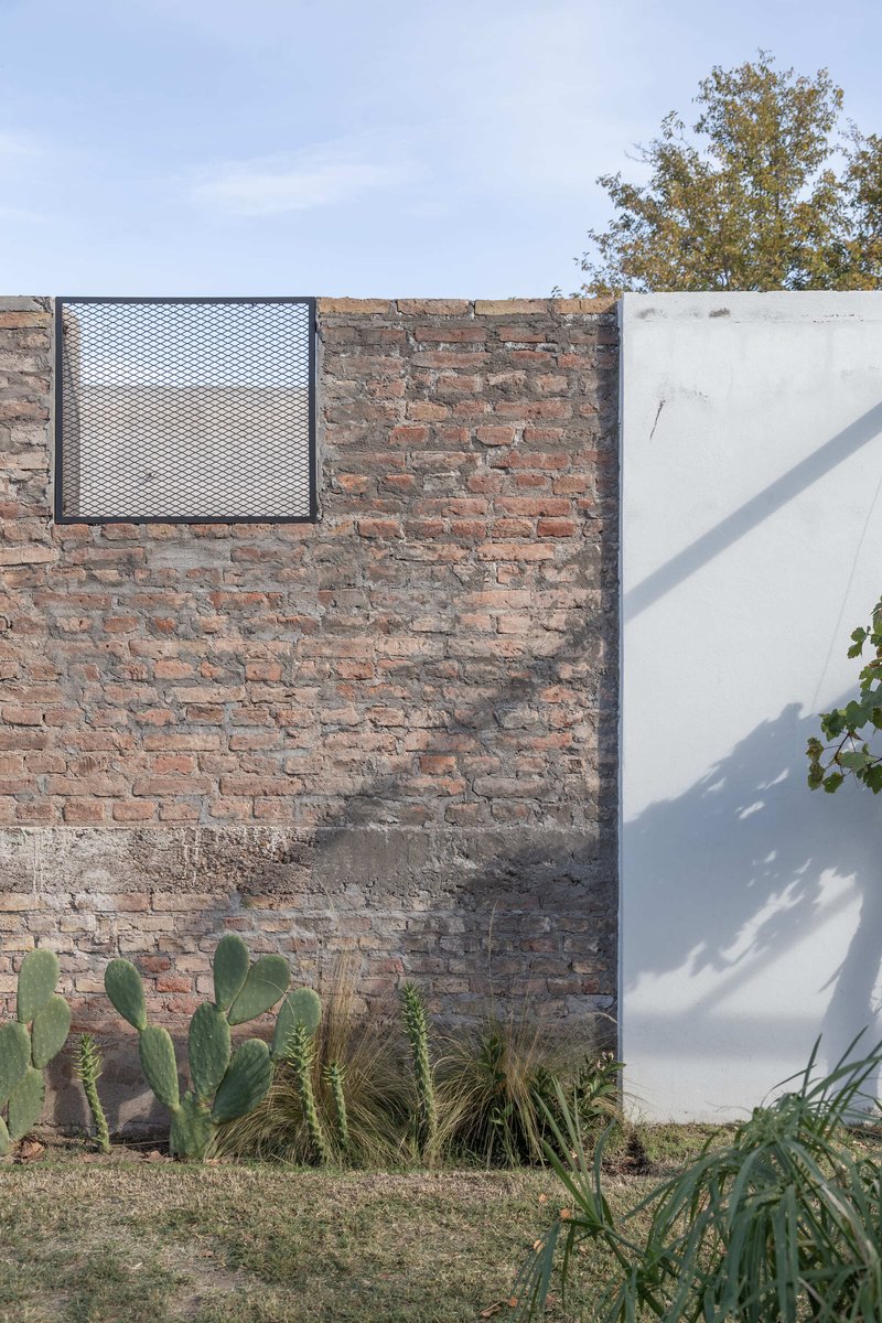 Weathered brick wall with square metal mesh window and planted bed of cacti and grasses below