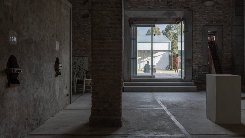 Interior gallery space with exposed brick columns and view through glazed opening to courtyard beyond