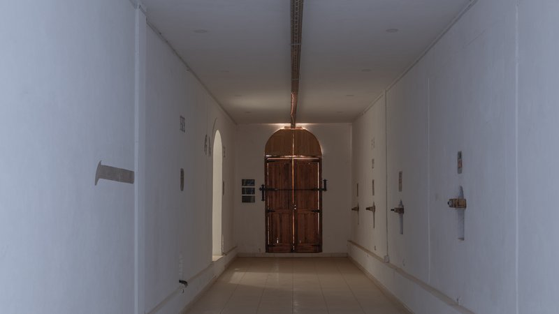 White plastered corridor with arched timber door and metal light fixture suspended from ceiling