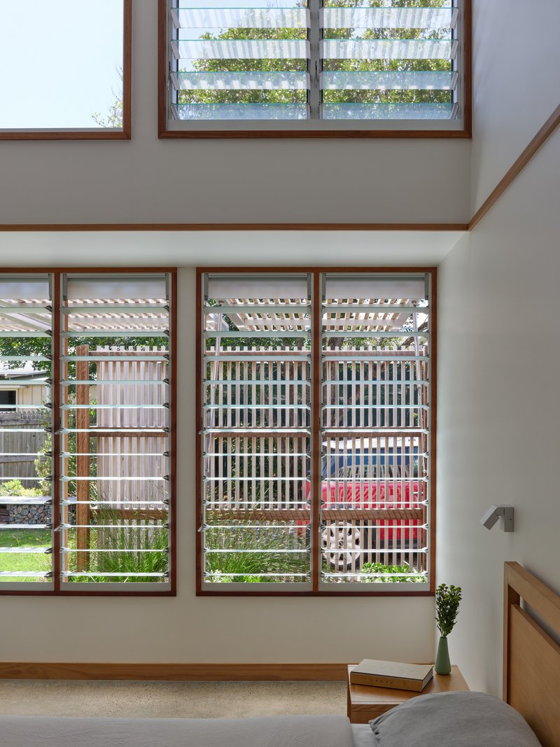 Double-height living space with timber-framed louvered windows filtering daylight into the interior
