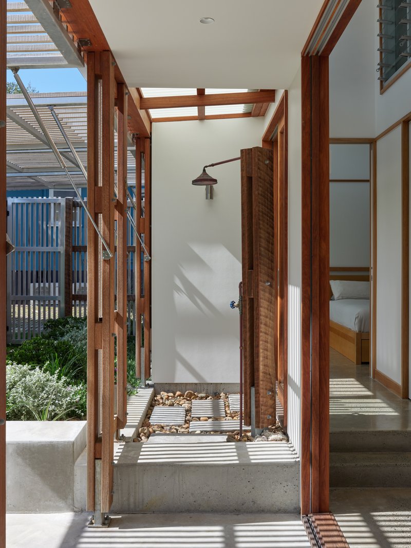 Outdoor shower enclosure with timber slat frame casting shadow patterns on concrete floor in bright daylight