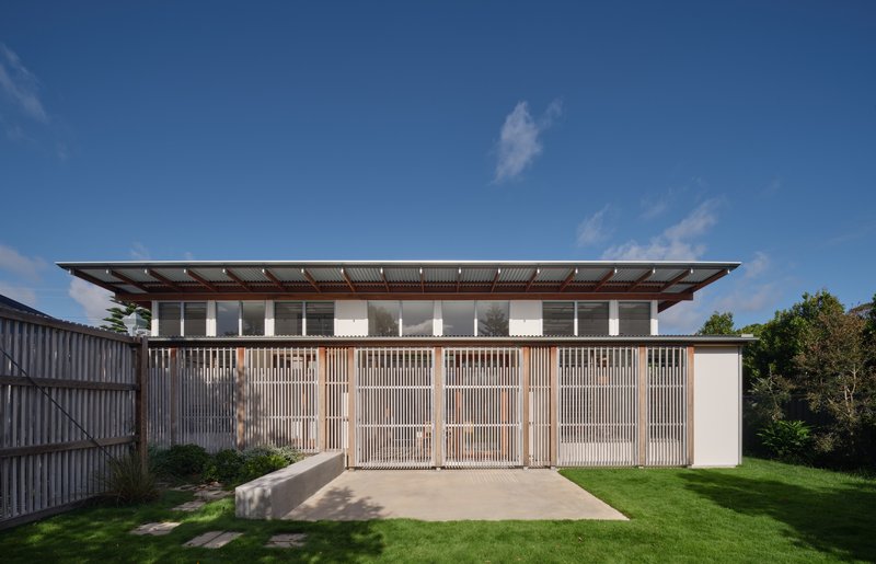 Front facade with vertical timber screens and expansive roof overhang above a grassed yard in afternoon light