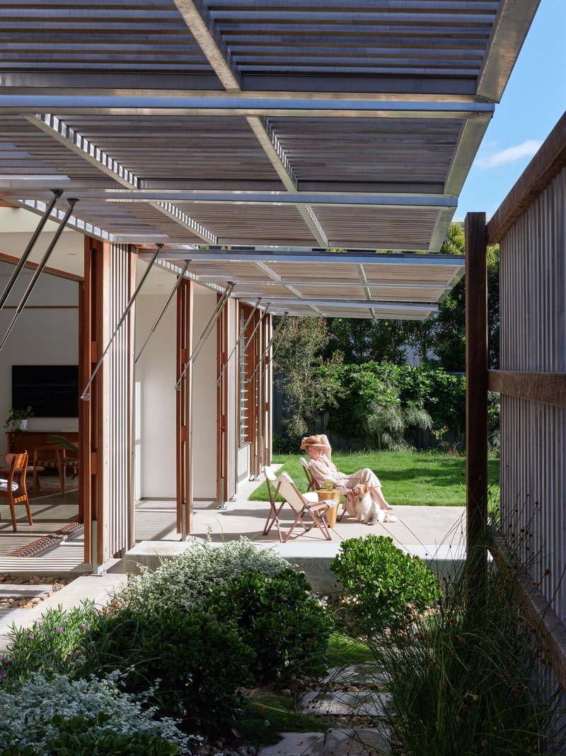Sheltered courtyard with slatted roof pergola where a person reclines beside a planted bed