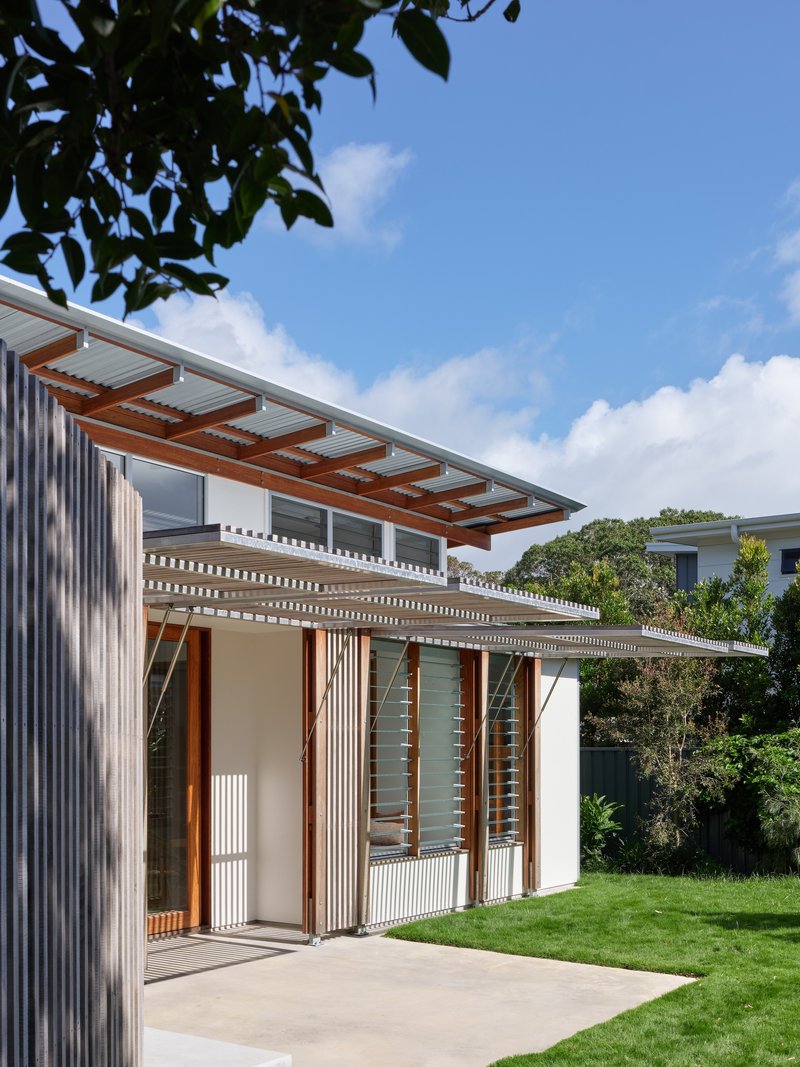 Exterior corner showing the cantilevered roof with exposed timber rafters and folding screen panels beneath overhanging foliage