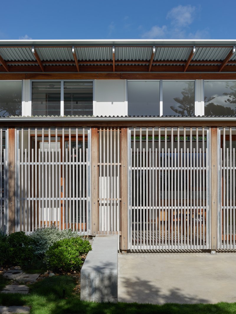 Exterior facade with vertical timber screening and corrugated roofing under a blue sky with low plantings