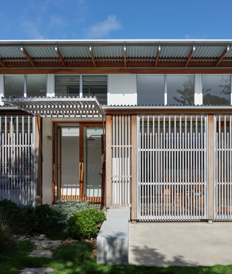 Entry with timber-framed glass doors and slatted screening beside a concrete path and lawn