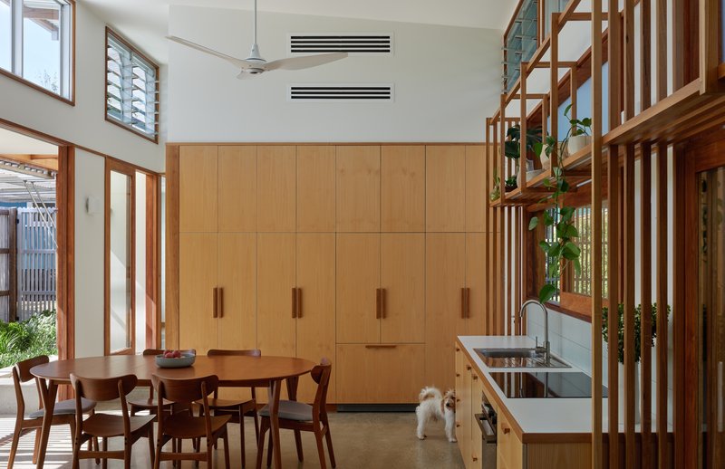 Open-plan dining area with timber cabinetry, timber staircase divider, and small dog on polished concrete