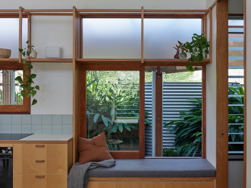 Built-in timber bench beneath clerestory windows overlooking a planted courtyard with corrugated metal fencing