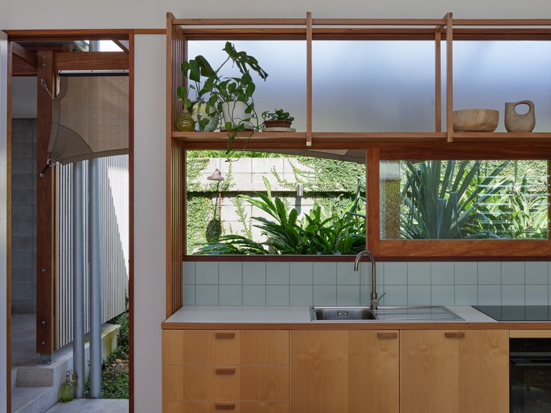 Kitchen with timber cabinetry and horizontal window band framing tropical plants in an adjacent courtyard