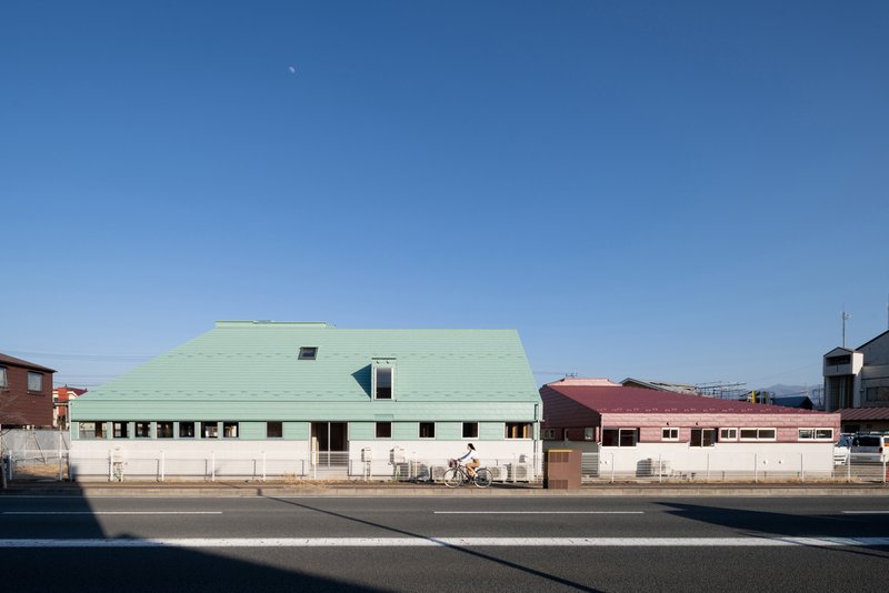 Street view of the building with a pale green pitched roof and continuous ribbon windows along the base