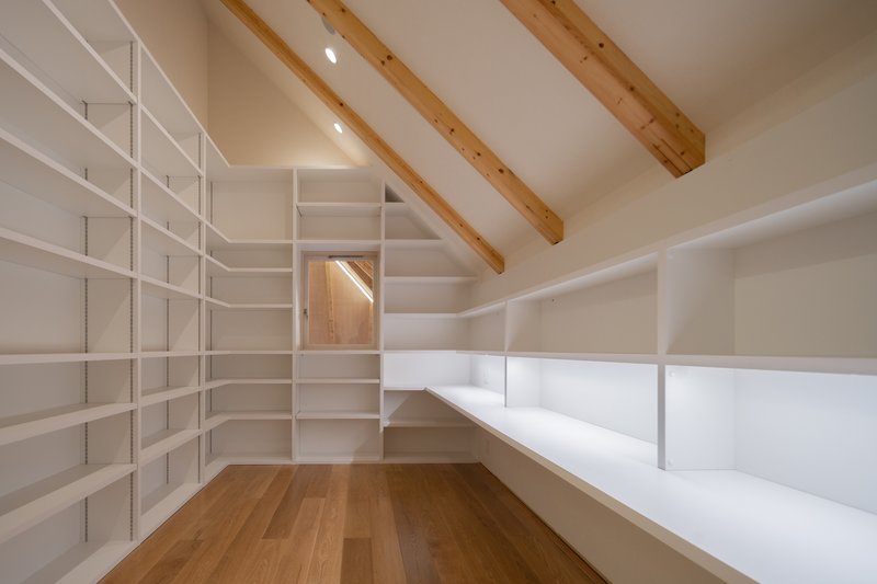 Corner of the library showing white modular shelving wrapping white walls beneath exposed timber beams