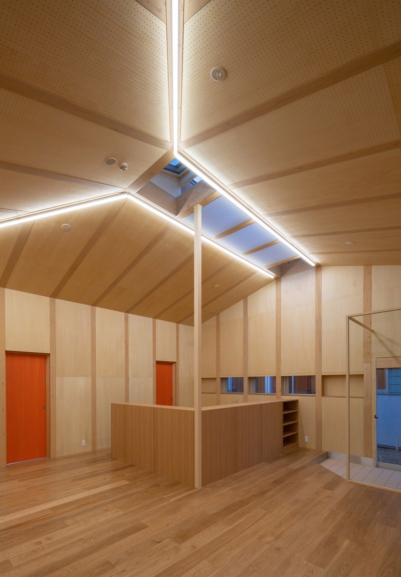 Double-height space with plywood paneling, gabled ceiling, and central island beneath a skylight at dusk