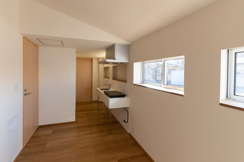 Compact kitchen with stainless steel range hood and horizontal windows overlooking neighboring rooftops