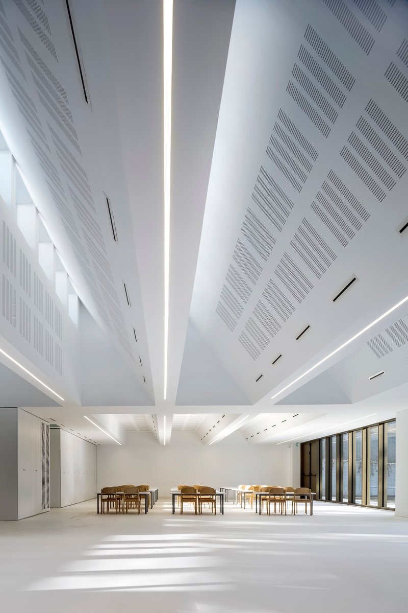 White ceiling with radial perforated panels and central skylight illuminating the white resin floor below