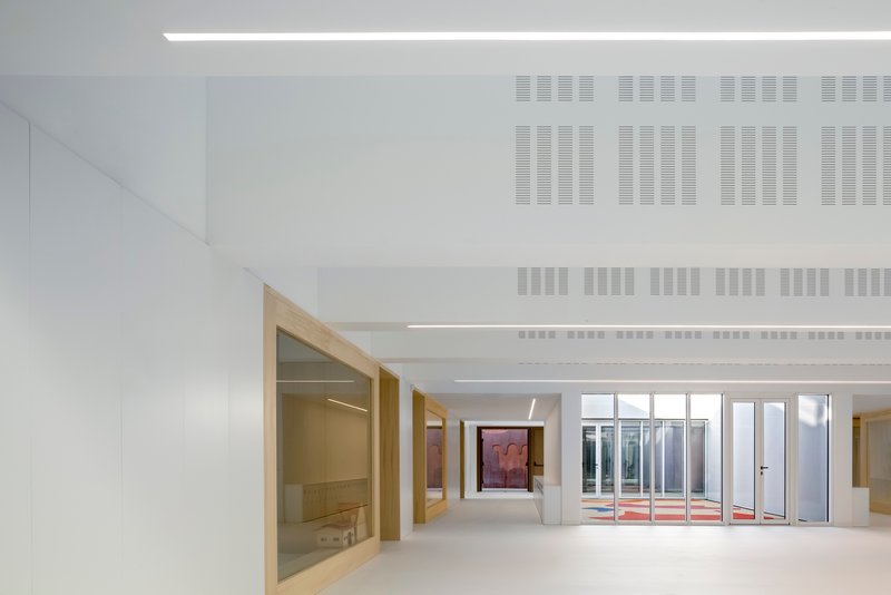 Corridor with timber door frames, perforated ceiling panels, and glazed courtyard opening at the end