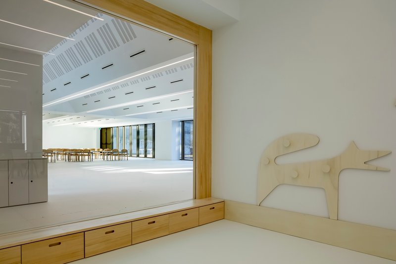 Built-in timber bench with storage drawers framing a view into a daylit multipurpose room