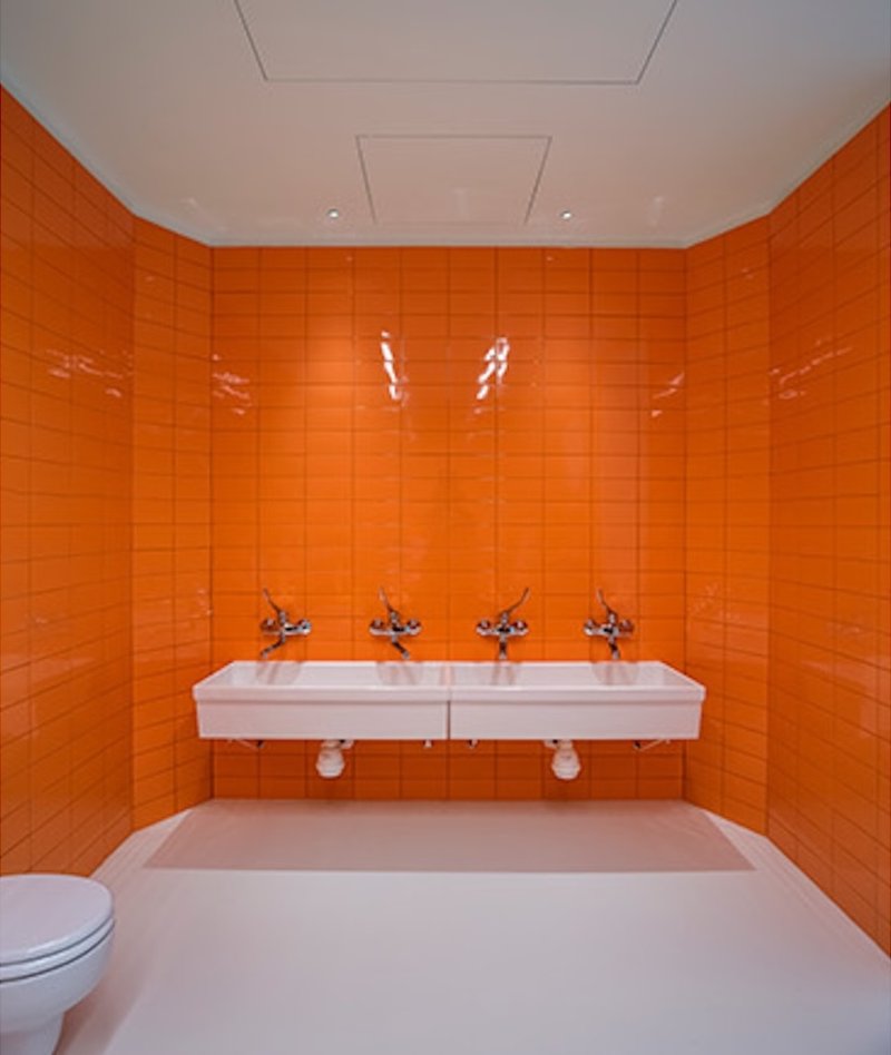 Restroom with glossy orange tile walls and twin wall-mounted sinks with chrome faucets