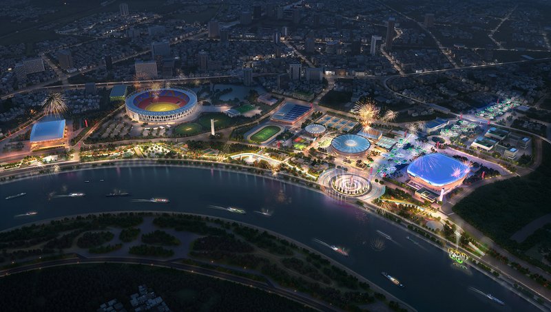 Nighttime aerial view of illuminated sports complex along curved riverbank with fireworks over domed pavilions