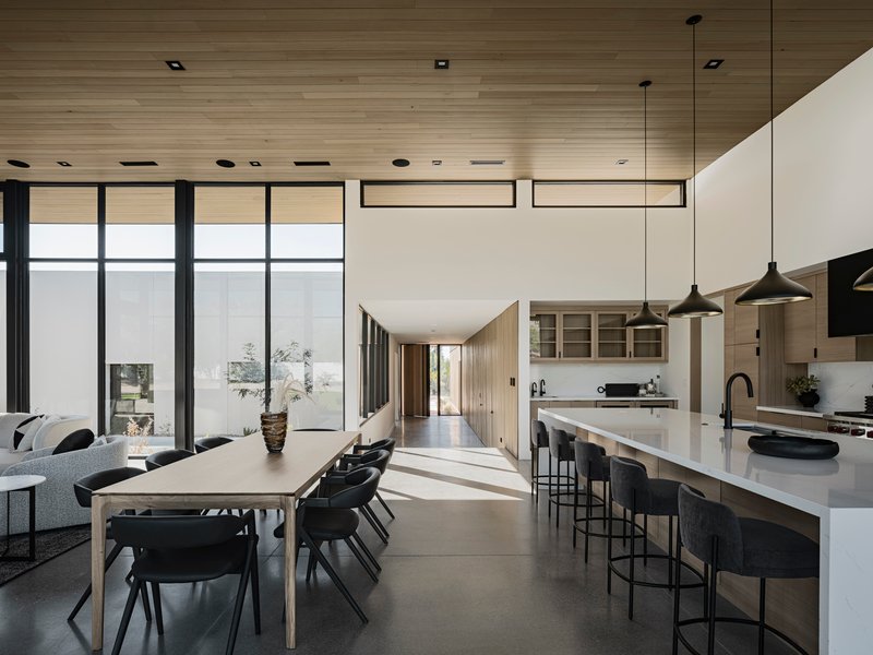 Combined dining and kitchen area with long white island under horizontal wood ceiling and clerestory windows above