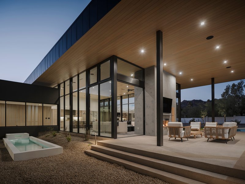 Covered terrace with timber soffit and black steel columns overlooking pool at dusk