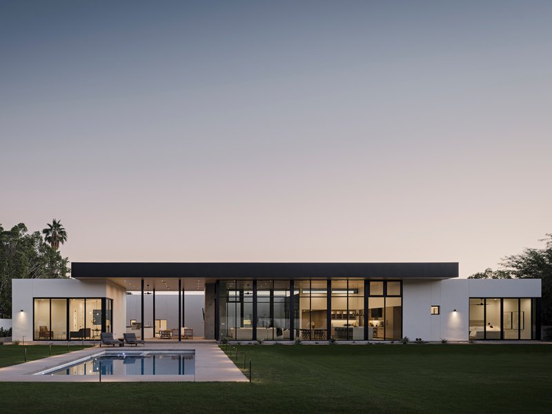 Garden elevation showing glass-walled living pavilion and swimming pool at dusk