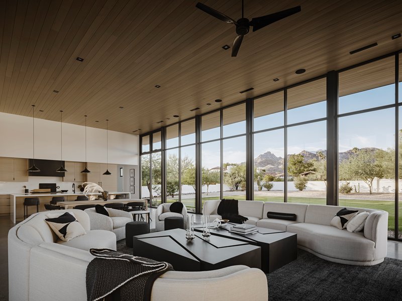 Living and kitchen area with wood-planked ceiling and full-height windows framing desert landscape