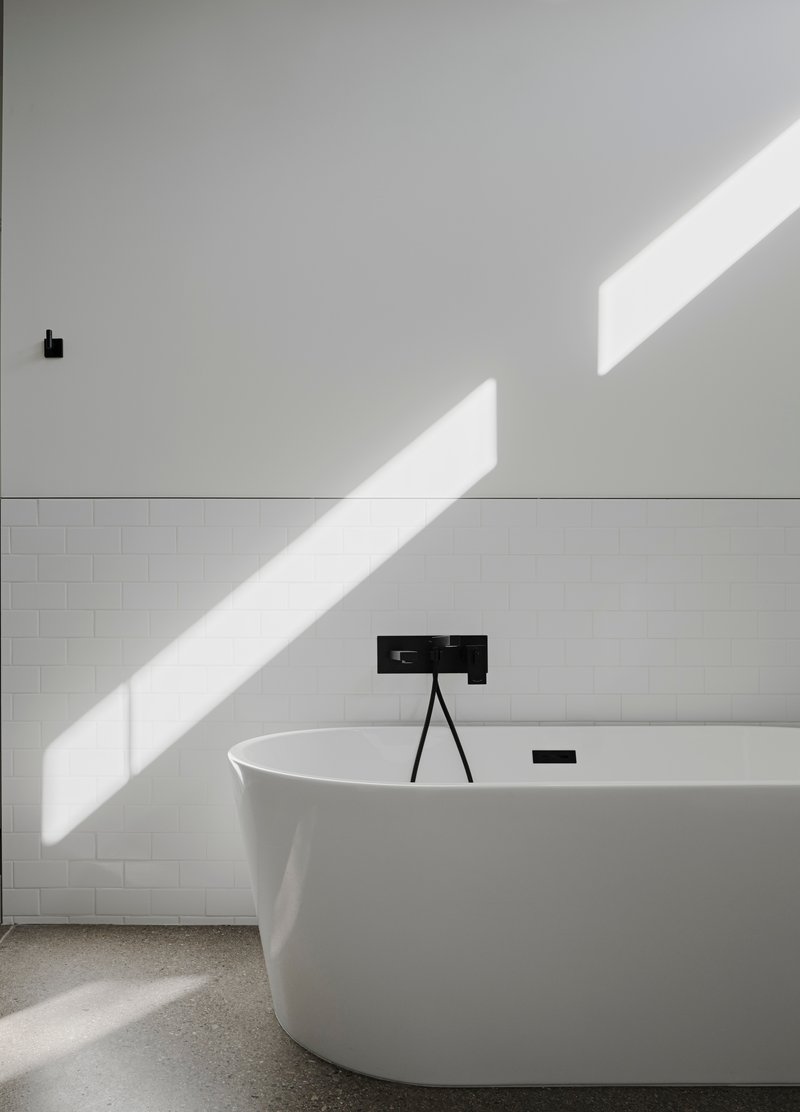 Freestanding white bathtub with black faucet under diagonal morning sunlight