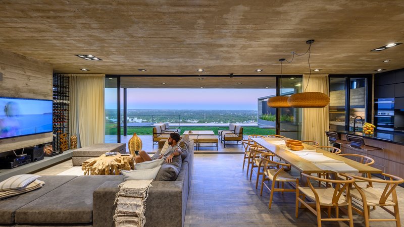 Open-plan living and dining area with timber ceiling and floor-to-ceiling glass facing the landscape at dusk