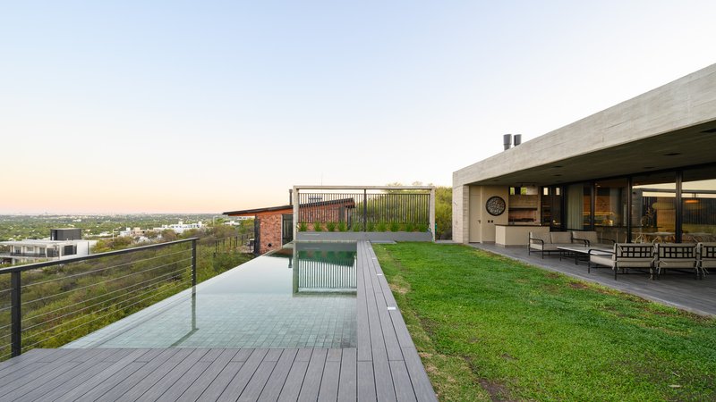 Rooftop terrace with lawn, timber deck, infinity pool and concrete canopy overlooking distant hills at sunset