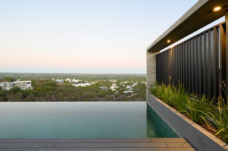 Infinity pool edge with vertical metal screen and timber deck at dusk with hills in the distance