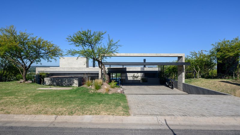 Street view of the flat-roofed residence with concrete volumes, vertical slat screen and mature trees