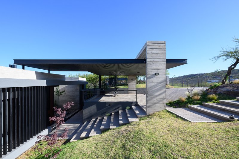 Cantilevered roof plane above board-formed concrete columns and a stepped entry pathway in full sun