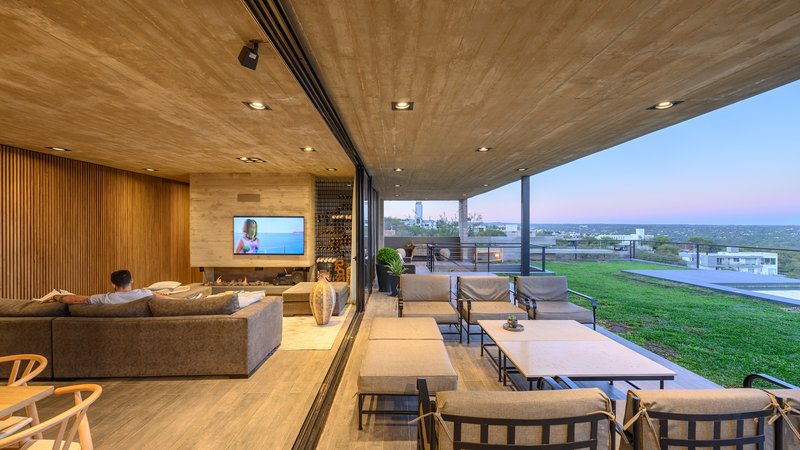 Open living space with timber-clad wall, timber ceiling, and floor-to-ceiling glazing overlooking lawn at dusk