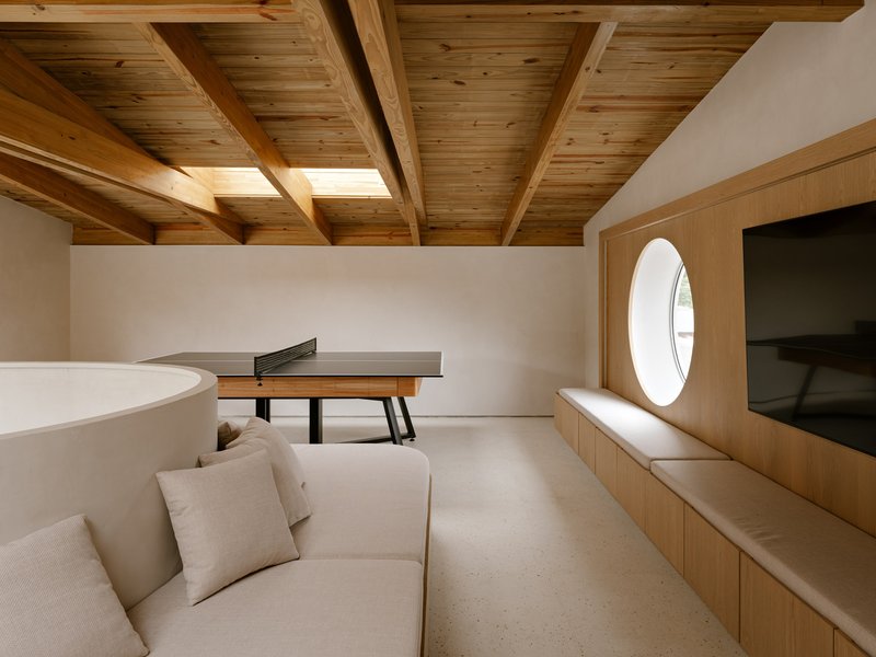Upper level room with exposed timber ceiling beams, a circular window and built-in bench seating