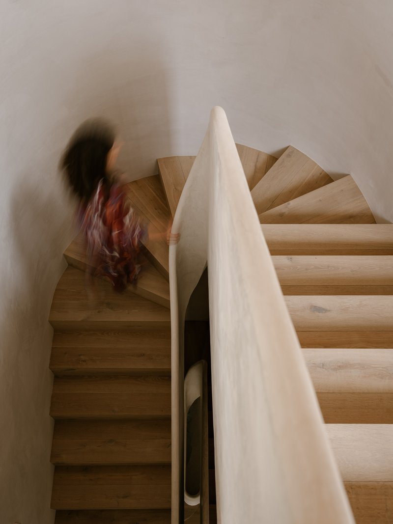 Timber spiral staircase with white plastered walls and a figure ascending in motion blur
