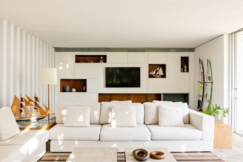 Living room with white storage wall featuring timber insets and vertical sheer curtains