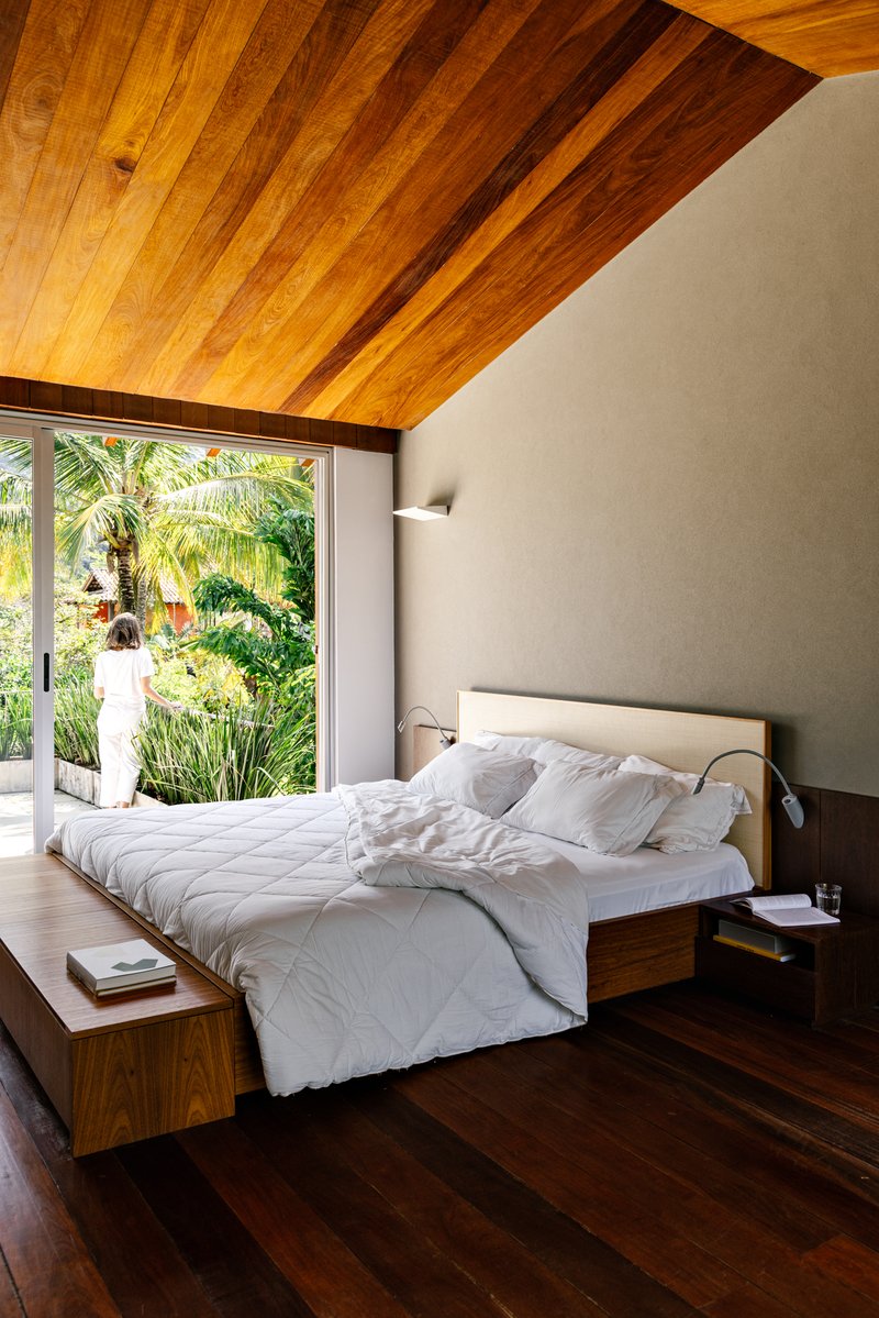Bedroom with sloped timber ceiling and glazed wall opening to garden with palm trees