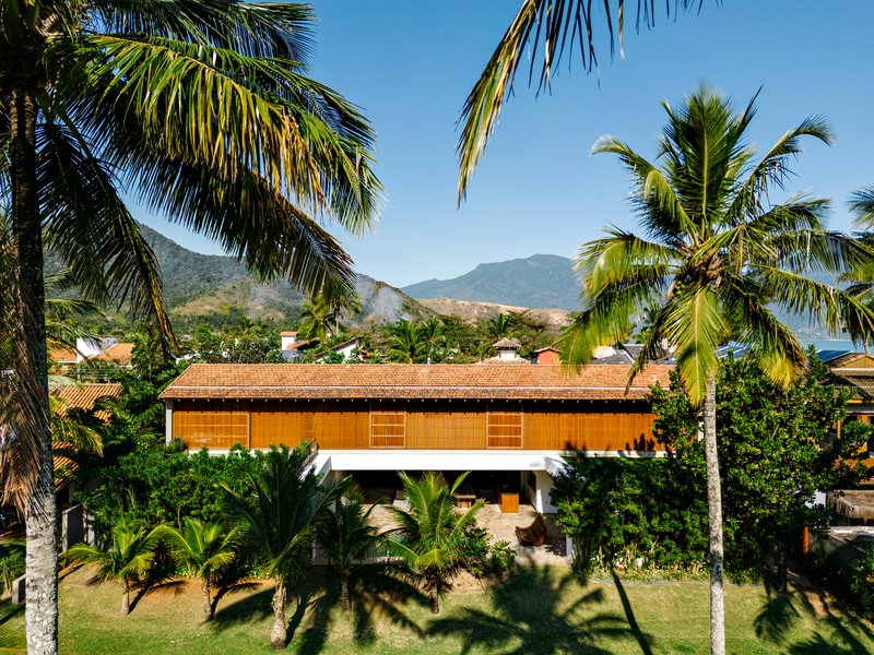Horizontal timber-screened facade with tile roof framed by palm trees and mountain range beyond