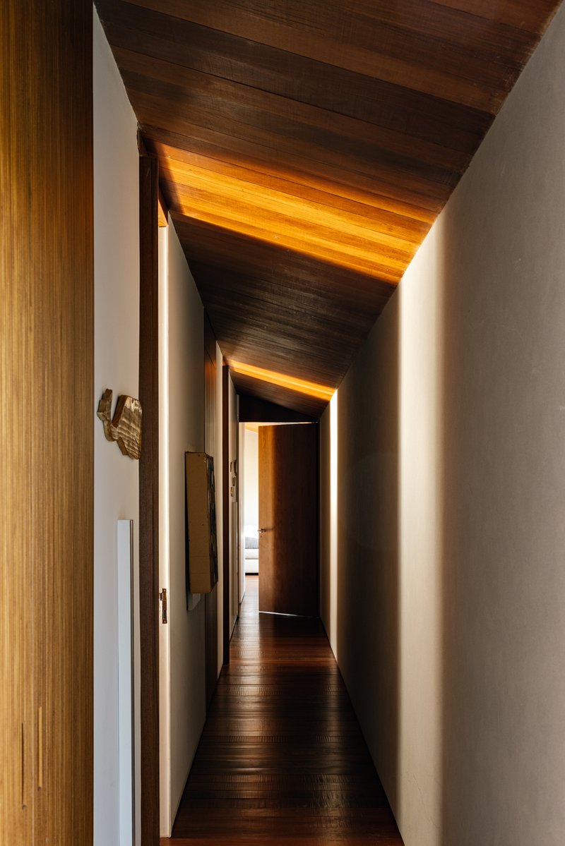 Corridor with folded timber ceiling planes and concealed lighting washing the white walls at dusk