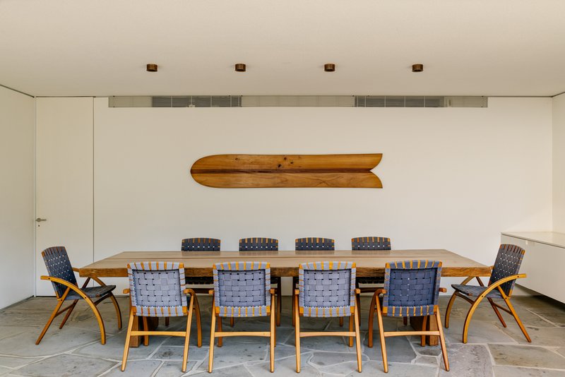 Dining area with timber table, woven chairs, and wooden canoe mounted on white wall