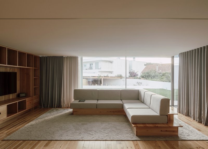 Living room with corner sofa facing full-height glazing overlooking lawn and neighboring rooftops