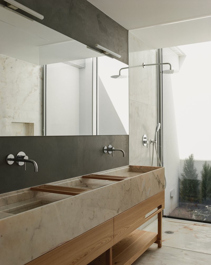 Bathroom vanity in veined stone with dual trough basins, timber cabinetry, and glass-enclosed shower opening to a courtyard